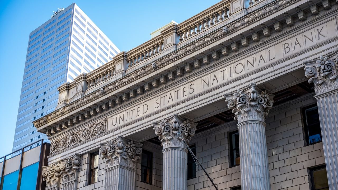 Exterior of historic national bank with decorative elements on classic columns located in city with modern building against blue sky