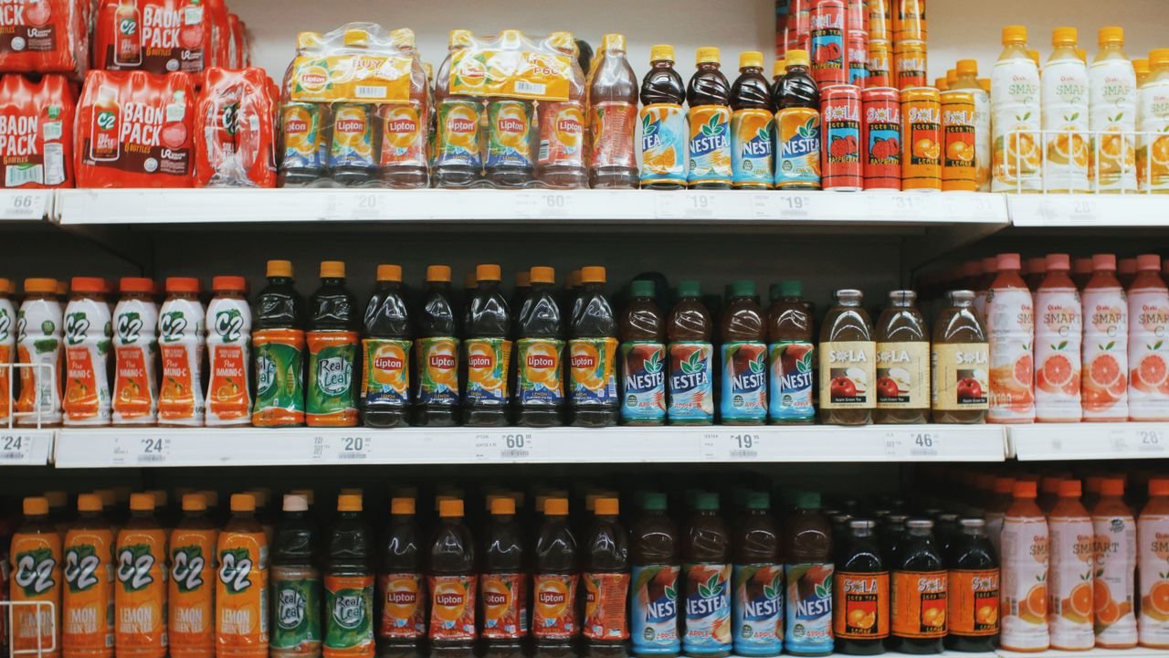 Rows of colorful plastic bottles with lemonades placed on light shelves in supermarket