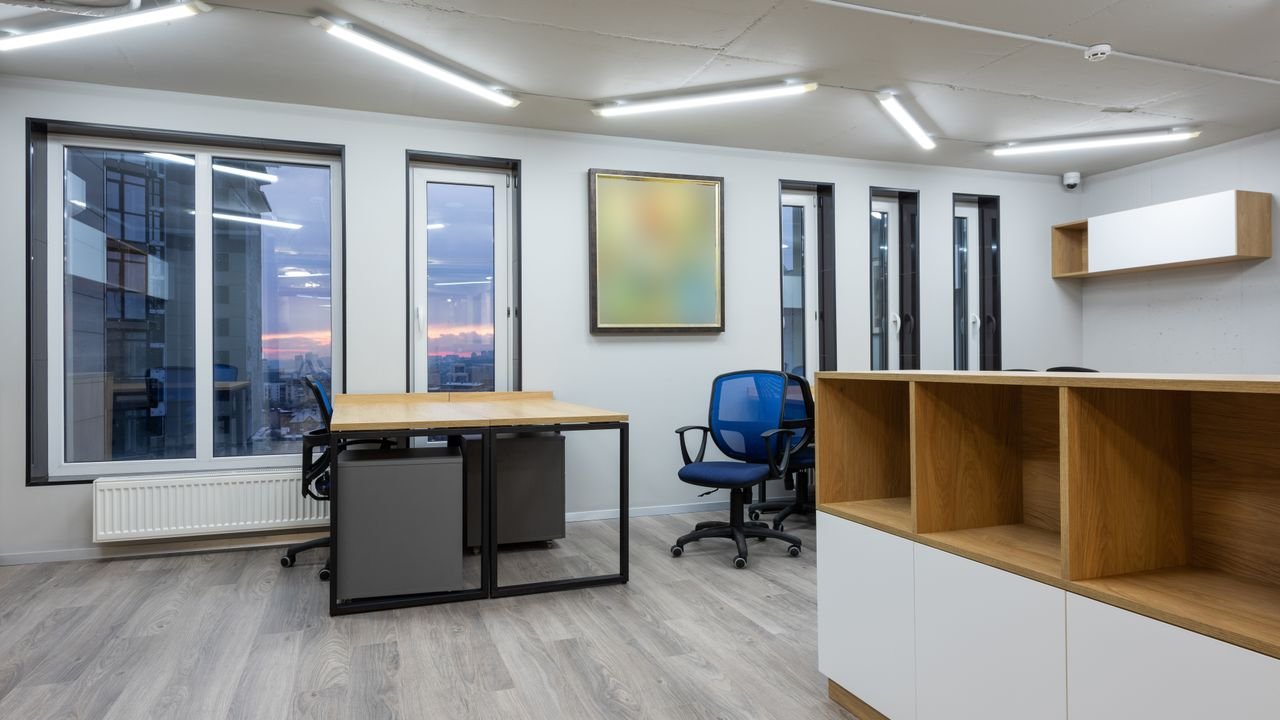 Interior of office with contemporary new wooden tables and chairs glowing by ceiling lamps