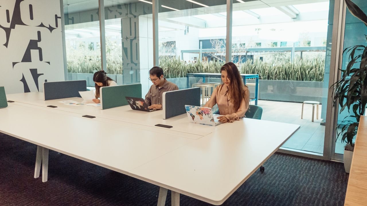 Contemporary office setting with professionals working on laptops at a shared desk.