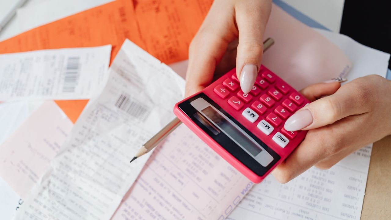 Hands using a pink calculator to manage expenses amidst various receipts and documents.