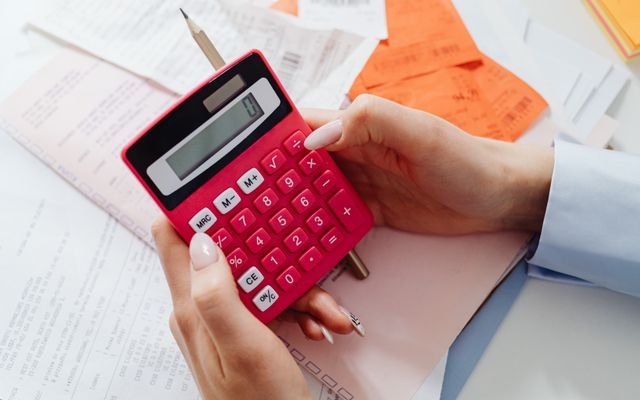 Close-up of hands holding a red calculator, managing finances with documents and receipts.