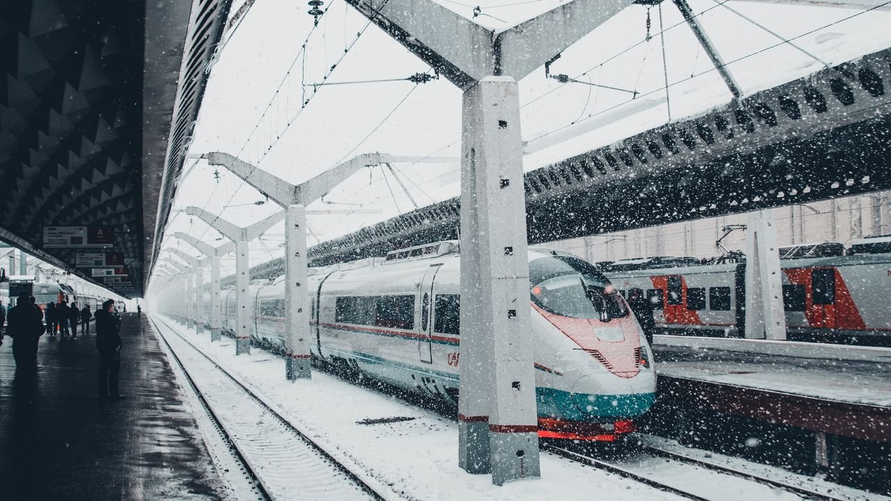 A sleek high-speed train at a snow-covered urban station during winter snowfall.