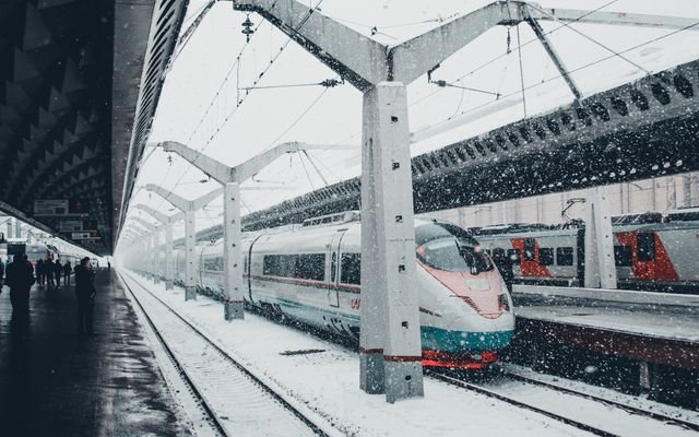A sleek high-speed train at a snow-covered urban station during winter snowfall.