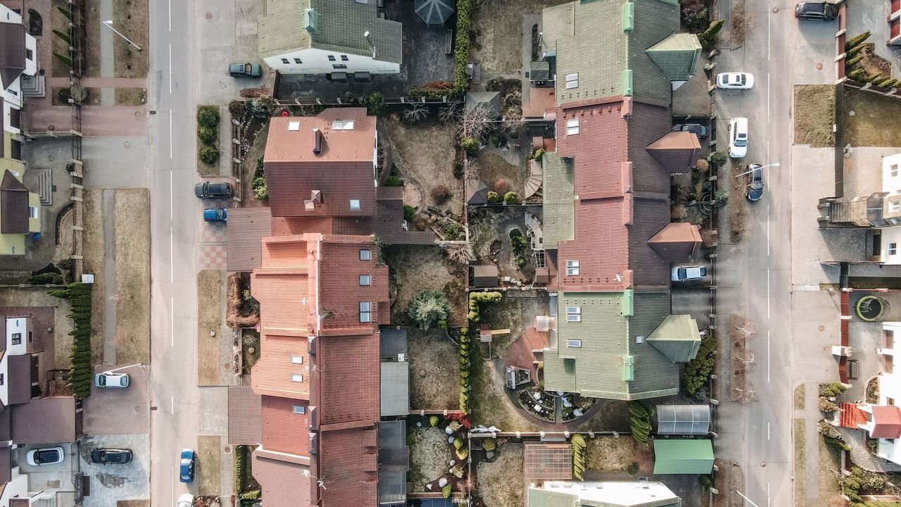 Aerial drone shot of a residential area with houses, streets, and parked cars.