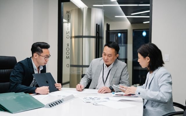 Business meeting with three professionals collaborating in a modern conference room setting.