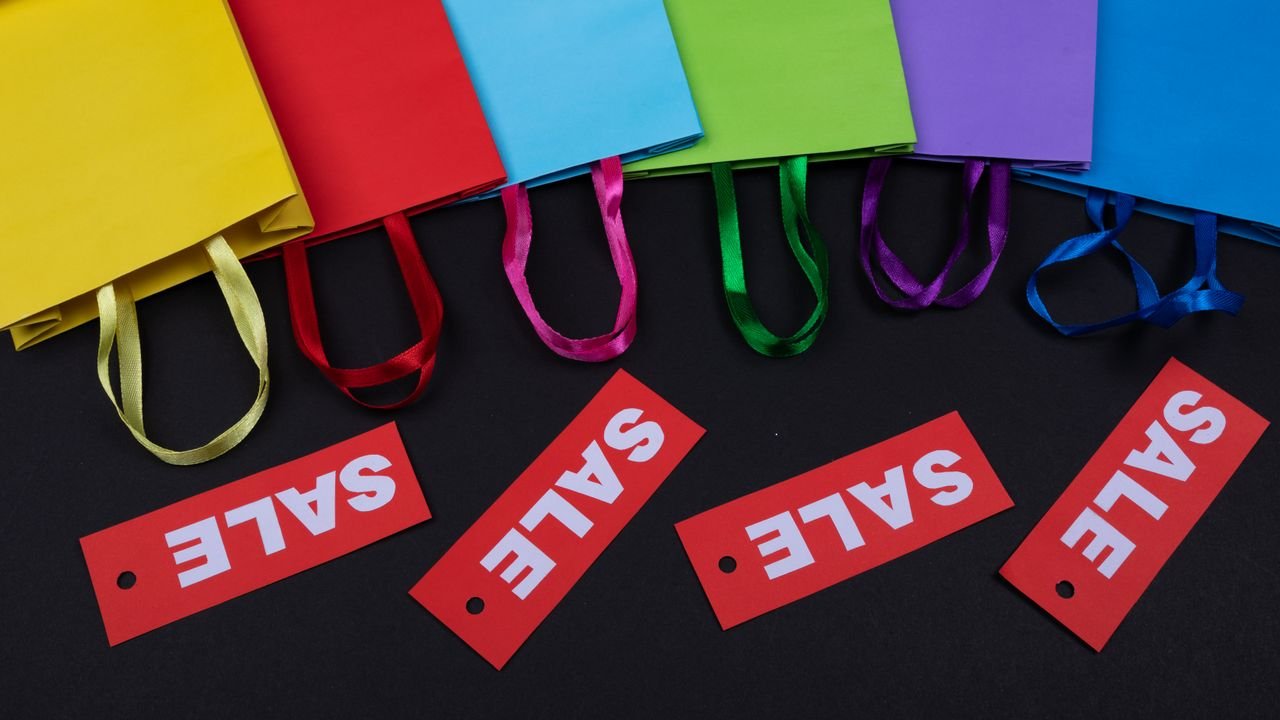 Vibrant paper bags with red sale tags on a black background, ideal for shopping promotions.