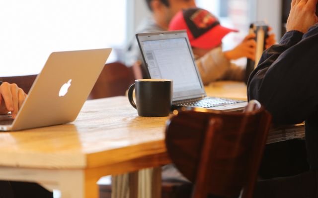 Group working in a cozy cafe with laptops and coffee mugs on a shared table.