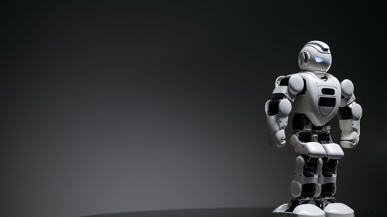 Compact humanoid robot toy standing on a reflective surface, exuding a futuristic vibe.