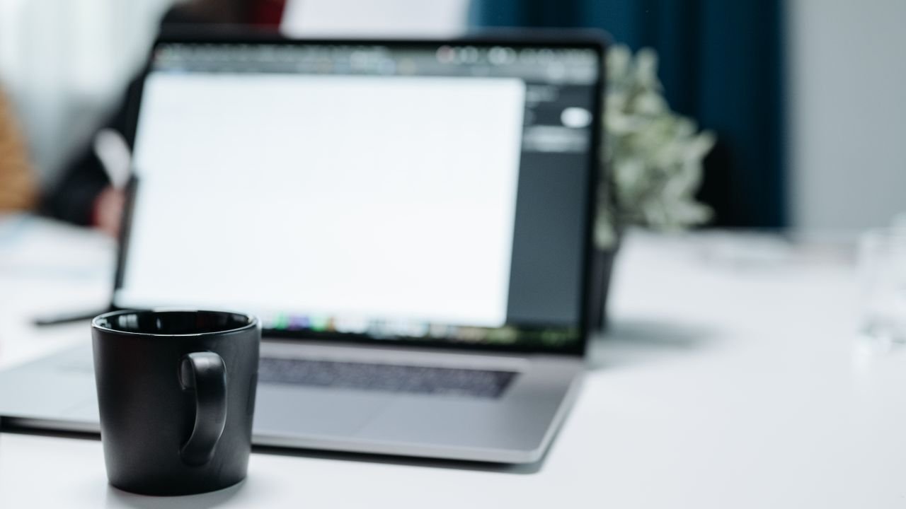 A black coffee mug on an office desk with a blurred laptop in the background.