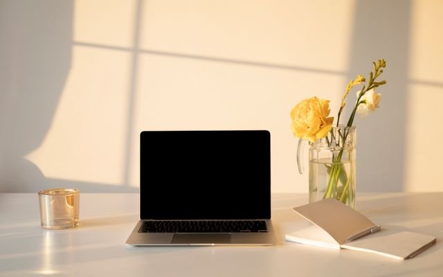 A serene minimalist workspace featuring a laptop, flowers, and a notebook, ideal for productivity and creativity.