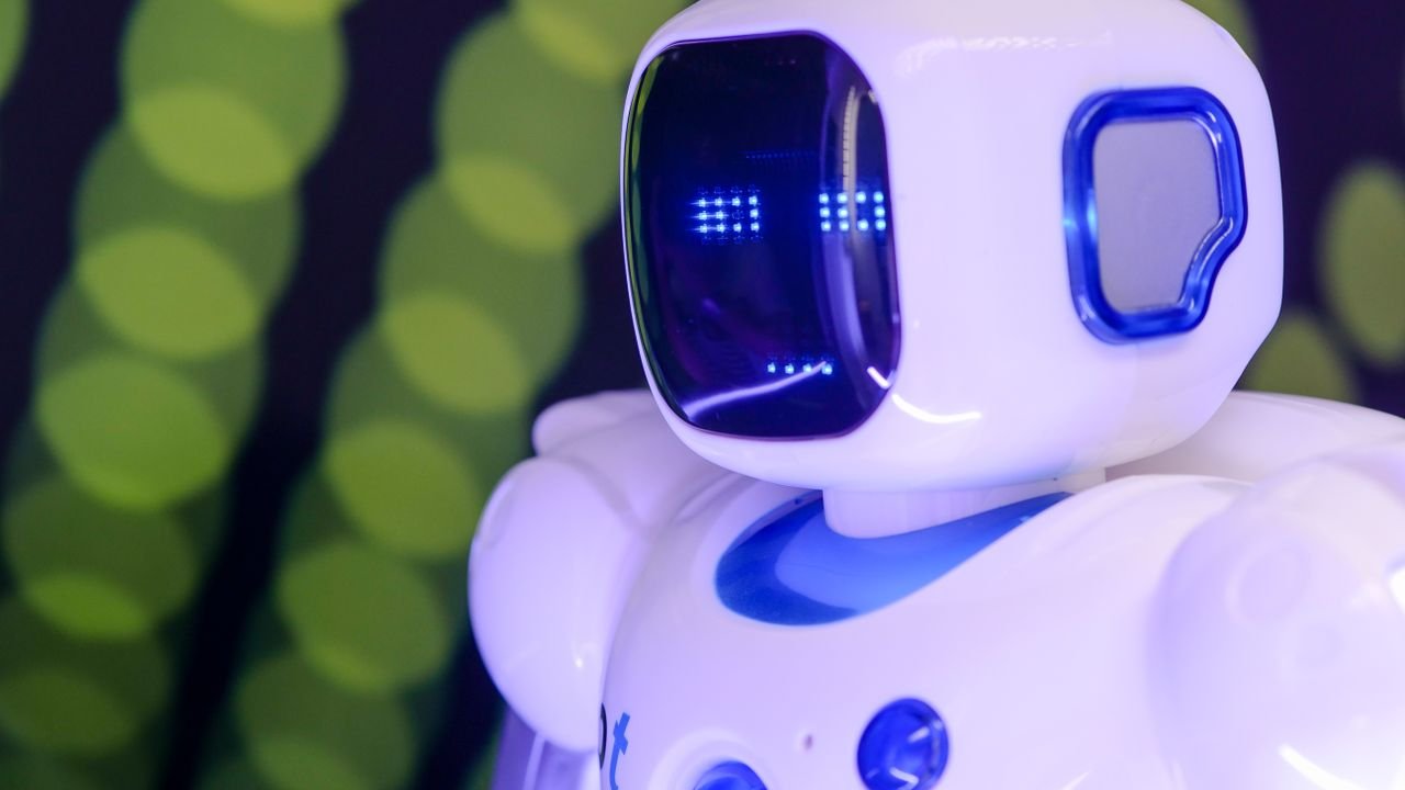 Close-up of a modern humanoid robot with glowing blue features on a green abstract background.