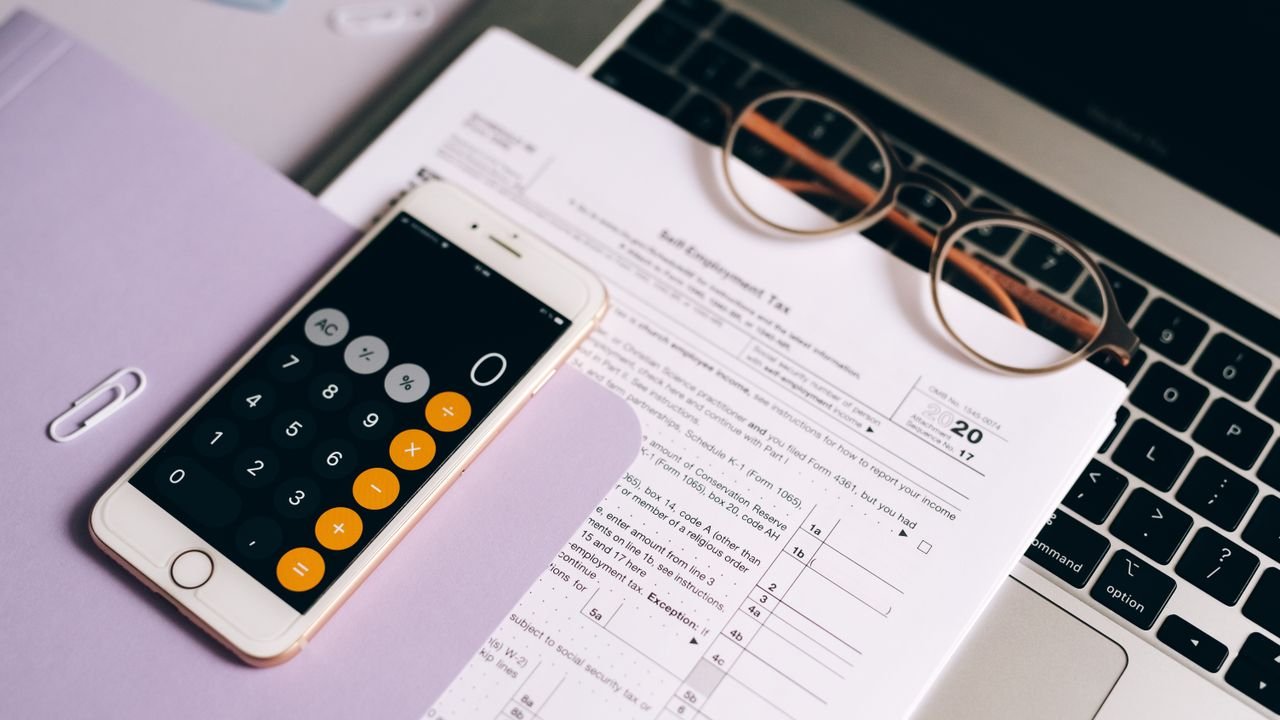 A smartphone with a calculator app on tax documents next to a laptop, emphasizing modern accounting.