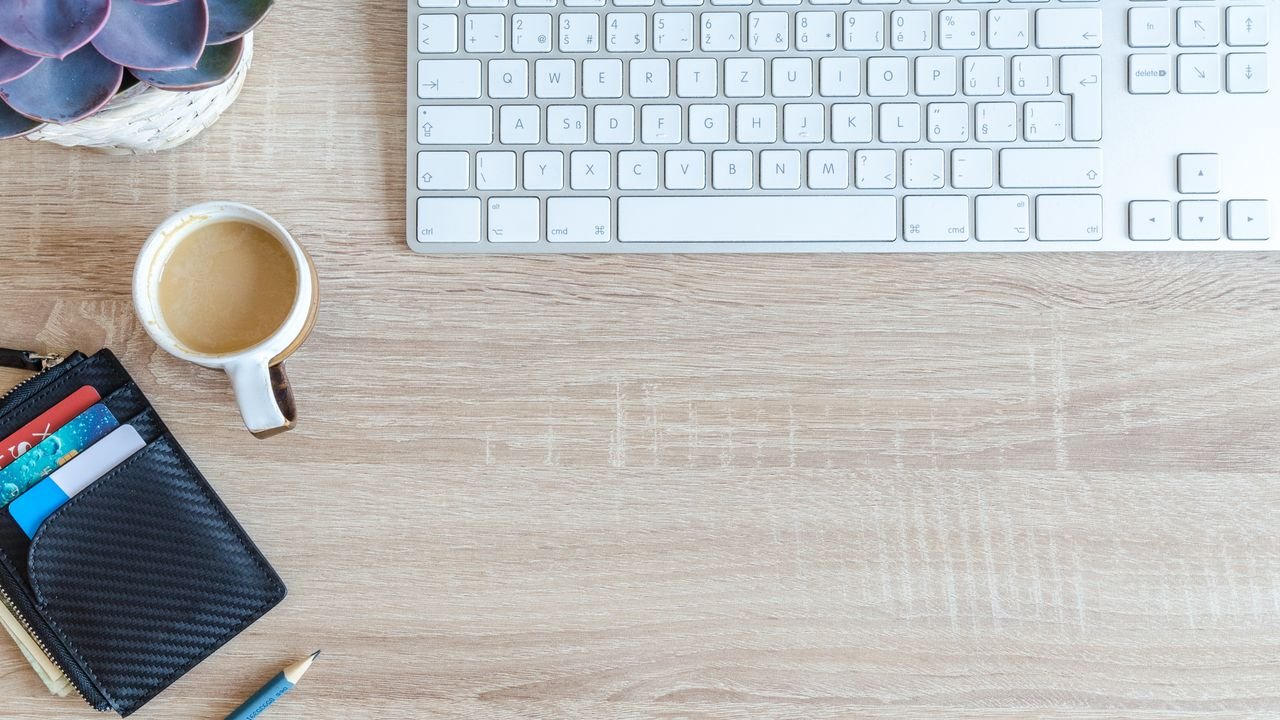 An organized workspace with a keyboard, coffee cup, wallet, and succulent plant on a wooden desk.