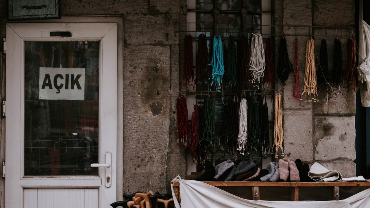 Outdoor display of colorful beads and accessories in front of an open door with Turkish sign.
