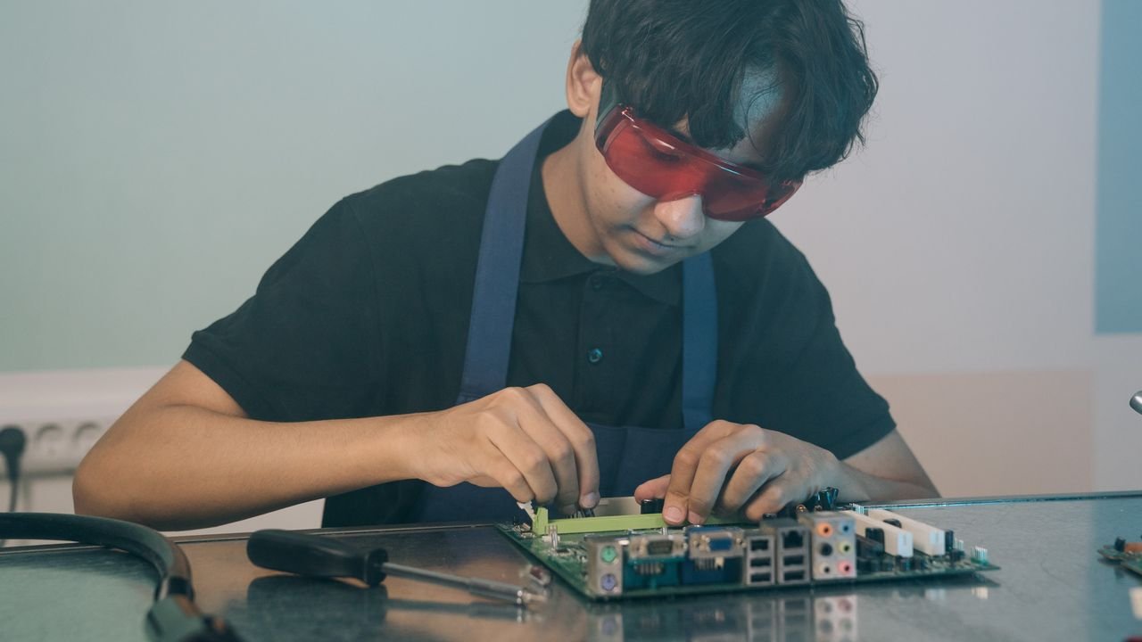 Young technician working with precision on a circuit board, demonstrating focused attention and technical skill indoors.