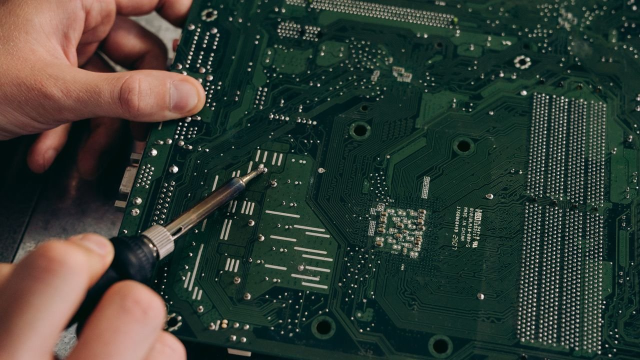 Hands soldering a motherboard with precision demonstrating electronics repair skills.