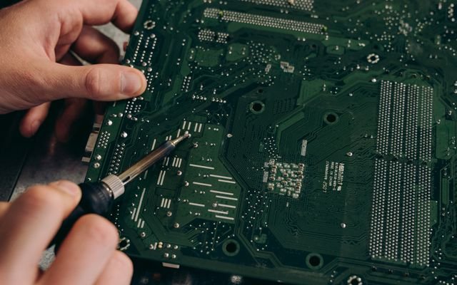 Hands soldering a motherboard with precision demonstrating electronics repair skills.