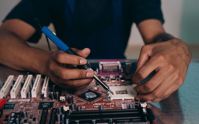 Engineer skillfully soldering components on a motherboard in a tech workshop.