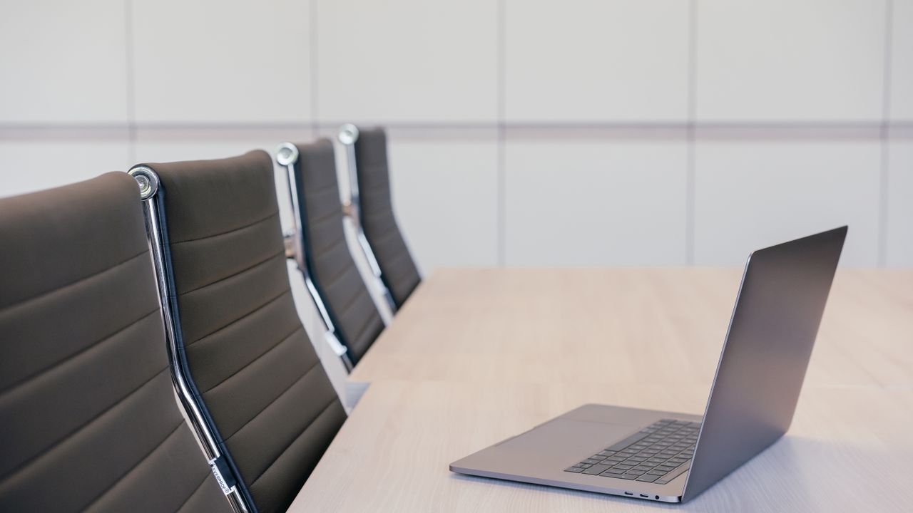 Minimalist office setup featuring a sleek laptop and stylish office chairs at a wooden table.