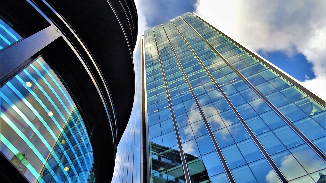 Low angle view of modern glass buildings with blue skies and clouds reflected in windows.
