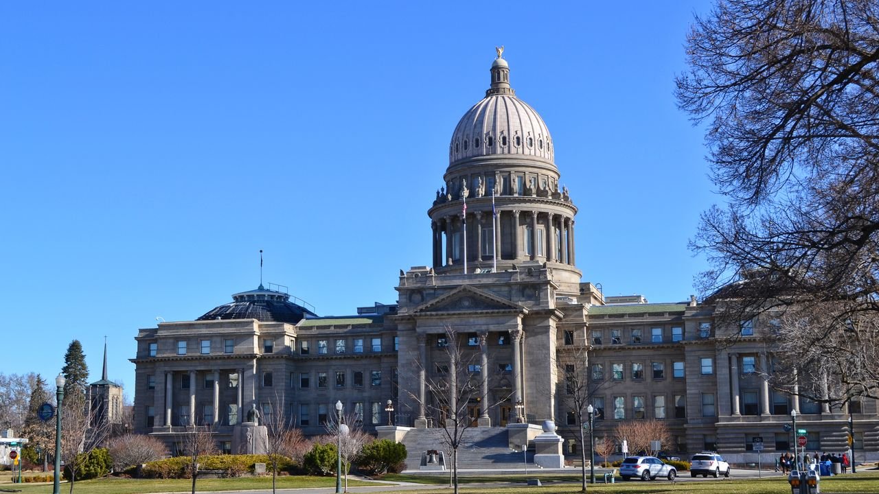 The Idaho State Capitol Building stands majestically under a clear blue sky with surrounding gardens.