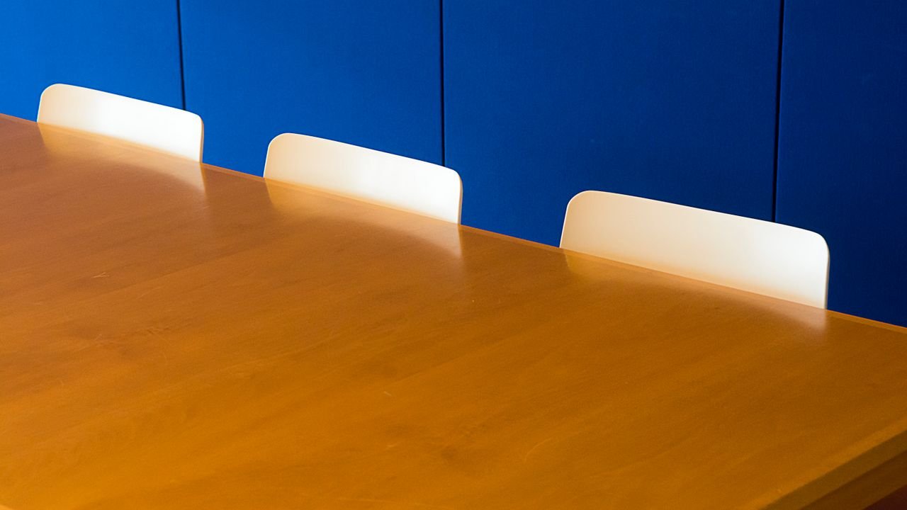 A clean and modern indoor meeting room with a wooden table against a blue wall.