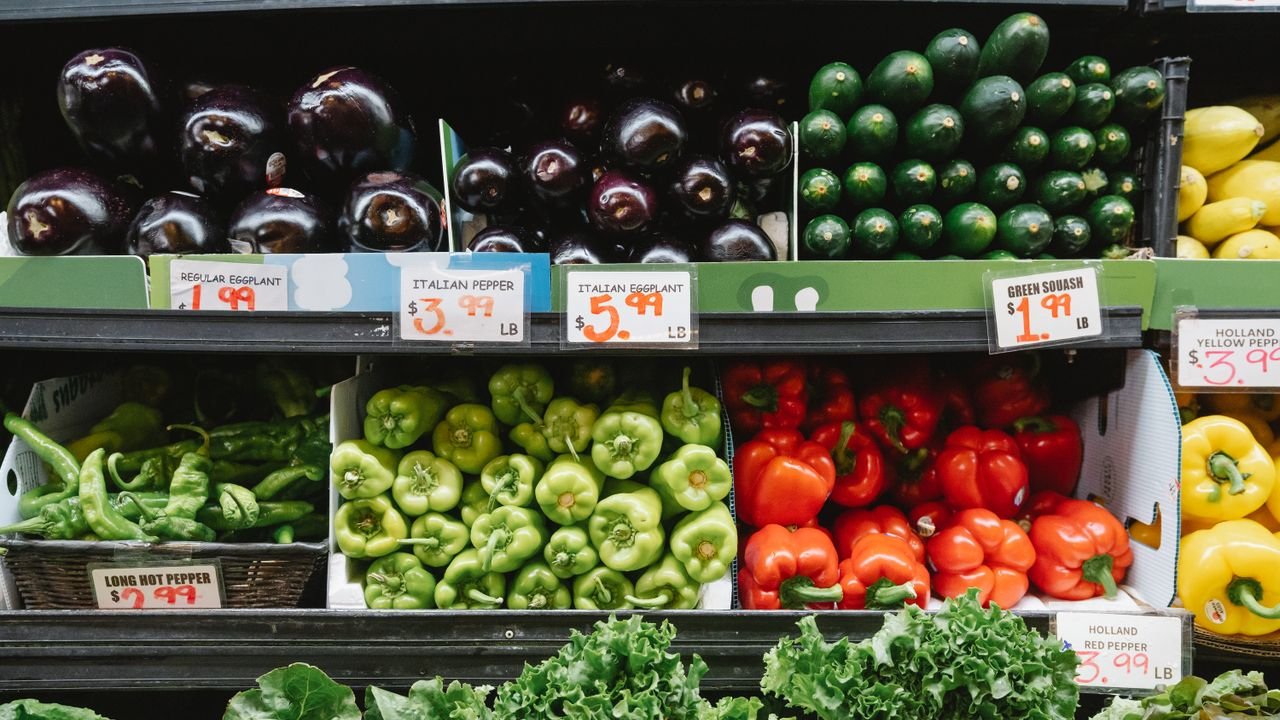 Colorful assortment of vegetables on display in a supermarket, featuring peppers, eggplants, and squash.
