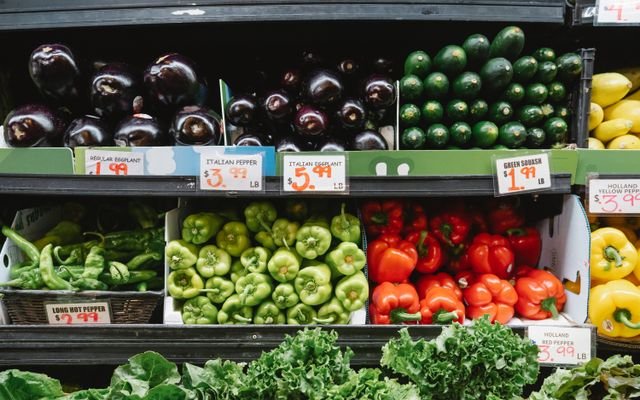 Colorful assortment of vegetables on display in a supermarket, featuring peppers, eggplants, and squash.